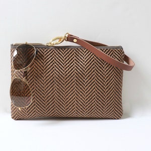 May include: A brown and black woven clutch bag with a brown leather strap and a pair of sunglasses inside.