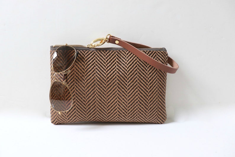 May include: A brown and black woven clutch bag with a brown leather strap and a pair of sunglasses inside.