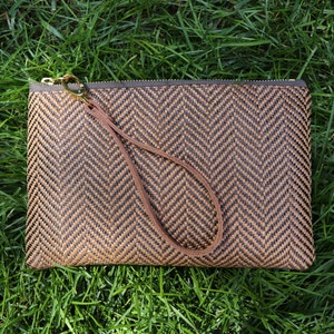 Lifestyle photo of brown woven zippered wristlet on green grass.