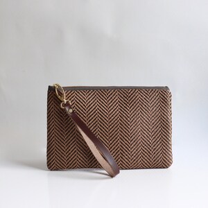 May include: A brown and black herringbone clutch with a brown leather strap.