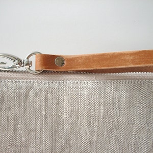 May include: A small, light gray linen pouch with a brown leather strap and a silver clasp. The pouch has a zipper closure.