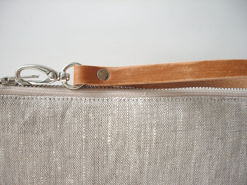 May include: A small, light gray linen pouch with a brown leather strap and a silver clasp. The pouch has a zipper closure.