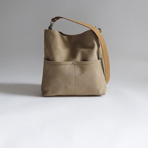 May include: A beige canvas tote bag with a brown leather strap and a front pocket.
