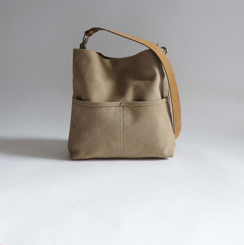 May include: A beige canvas tote bag with a brown leather strap and a front pocket.