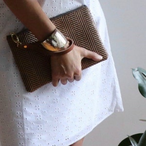 May include: A brown woven clutch with a herringbone pattern. The clutch has a leather strap and a gold metal clasp.