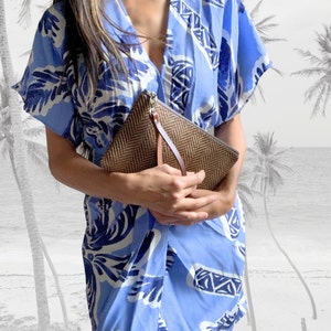May include: A woman wearing a blue and white patterned dress holds a brown woven clutch with a leather strap.