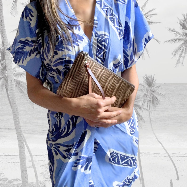 May include: A woman wearing a blue and white patterned dress holds a brown woven clutch with a leather strap.