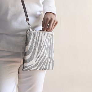 Model holding zebra print crossbody purse in gray and natural colors.