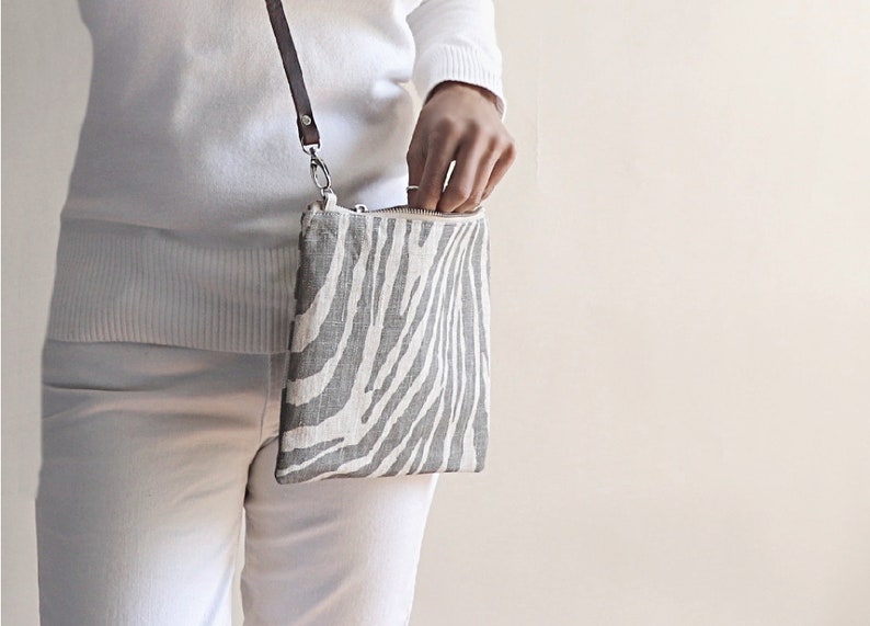 Model holding zebra print crossbody purse in gray and natural colors.