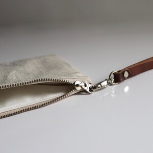 May include: A beige linen zippered pouch with a brown leather strap and a silver clasp.