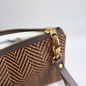 May include: A brown and black woven clutch with a gold zipper and a brown leather strap.