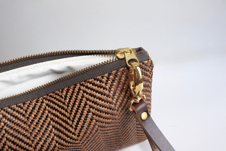 May include: A brown and black woven clutch with a gold zipper and a brown leather strap.
