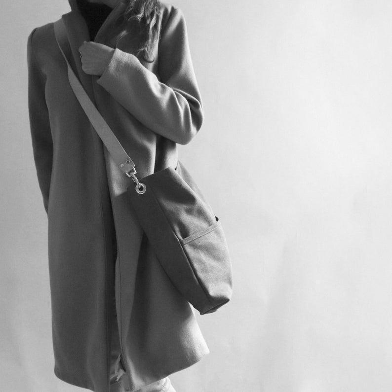 May include: A gray coat with a long, brown leather strap and a large, dark gray tote bag.
