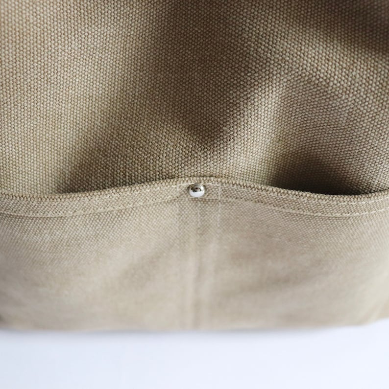 May include: Close-up of a beige canvas tote bag with a small silver rivet on the pocket.