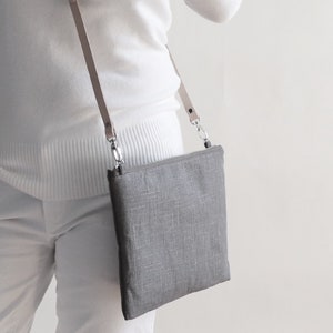 Model holding gray linen crossbody bag with adjustable leather strap.
