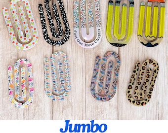 May include: A collection of jumbo paperclip bookmarks in various patterns, including apples, black and white swirls, and leopard print. One bookmark has the text "Just One More Chapter". The bookmarks are on a light wood surface.