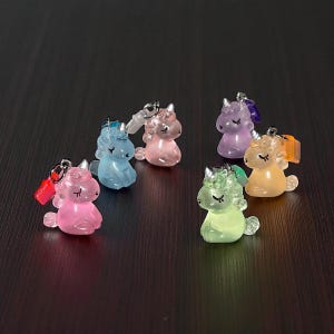 Op de afbeelding: Een verzameling van zes miniatuur eenhoornfiguren in pastelkleuren, waaronder roze, blauw, paars en geel. Elke eenhoorn heeft een kleine zilveren lus voor bevestiging, wat suggereert dat het bedels of sleutelhangers zijn. De eenhoorns zitten.