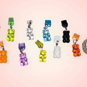 Könnte beinhalten: Sortiment an bunten Gummibärchen-Anhängern mit silbernen Metallverschlüssen. Die Anhänger sind in verschiedenen Farben, darunter Orange, Gelb, Grün, Blau, Lila, Rosa und Weiß.