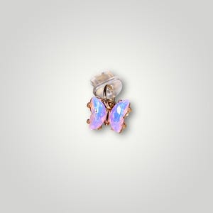 May include: A small gold butterfly charm with iridescent pink and purple wings. The charm is attached to a clear plastic earring back.