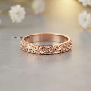 May include: Rose gold ring with intricate floral scrollwork and a beaded border. The ring is a band style, with a polished finish. The ring is a beautiful piece of jewelry.