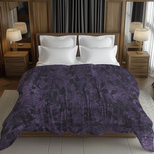 Op de afbeelding: Een bed met witte kussens en een donkerpaarse deken. De deken heeft een bloemenpatroon in een donkerdere tint paars. Het bed staat in een kamer met houten lambrisering, gordijnen en lampen op nachtkastjes.