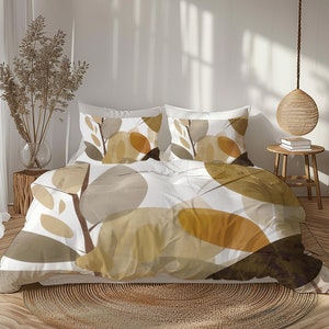 Può includere: Un copripiumino bianco con un motivo astratto di foglie marroni e gialle. Il copripiumino è su un letto con due federe abbinate. Il letto è in una camera da letto con pavimento in legno e un cesto di vimini.