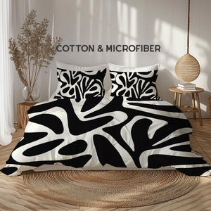 Op de afbeelding: Een bed met een zwart-wit abstract patroon beddengoed set. De set bevat een dekbedovertrek en twee kussenslopen. De tekst "COTTON & MICROFIBER" is zichtbaar.