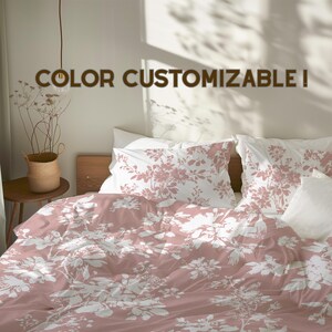 Könnte beinhalten: Ein Bett mit einer rosa Bettdecke mit Blumenmuster und passenden Kissenbezügen. Die Bettwäsche hat ein weißes Blumendesign auf rosa Hintergrund. Der Text "COLOR CUSTOMIZABLE!" wird oben im Bild angezeigt.
