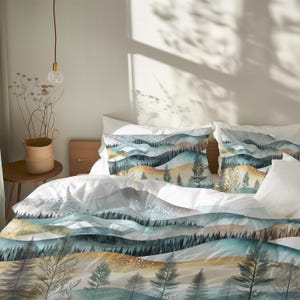 May include: Bed linen set with a watercolour landscape design. The duvet cover and pillowcases show a serene mountain scene in shades of blue, green, and gold. The design includes trees and rolling hills, creating a tranquil aesthetic for the bedroom.