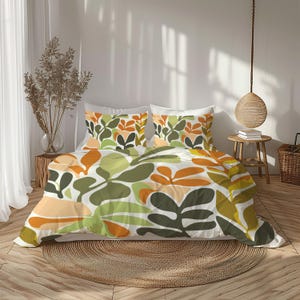 May include: A bed set featuring a duvet cover and two pillowcases. The bedding has a white background with a repeating pattern of large, abstract leaves in shades of green, orange, and yellow. The room has a neutral color palette.