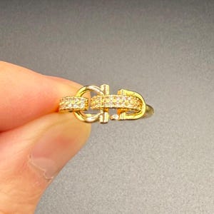 May include: Gold ring featuring a double interlocking design, embellished with small clear stones.