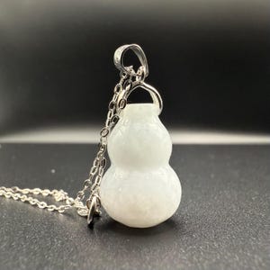 May include: A white gourd-shaped pendant necklace with a silver chain. The pendant has a smooth, rounded form with a slight texture. The silver chain is delicate and connects to the pendant at the top.