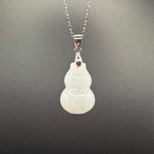 May include: A white jade gourd pendant necklace with a silver chain. The gourd-shaped pendant is smooth and translucent, with a subtle, natural pattern. The necklace is a delicate piece of jewelry.