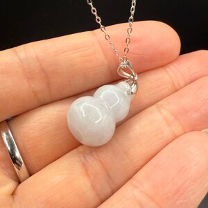 May include: A delicate silver necklace featuring a gourd-shaped pendant. The pendant is a pale, translucent color, with a smooth, polished surface. The necklace chain is thin and silver, complementing the pendant's subtle elegance.