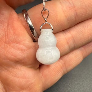 May include: A white gourd-shaped pendant necklace with a silver-colored bail and chain. The pendant is smooth and has a slightly translucent appearance. The necklace is shown against a neutral background.