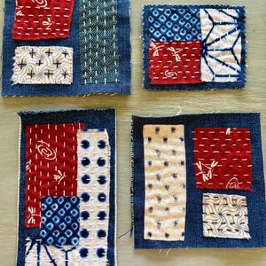 May include: Four denim fabric squares with various fabric patches in red, white, and blue, stitched with white thread. The patches feature geometric and floral patterns, showcasing a handcrafted aesthetic.