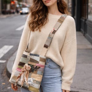 May include: A patchwork shoulder bag with a floral embellishment. The bag features a variety of fabric patches in muted tones of beige, green, and pink. The strap is also patchwork. The bag is worn over the shoulder.