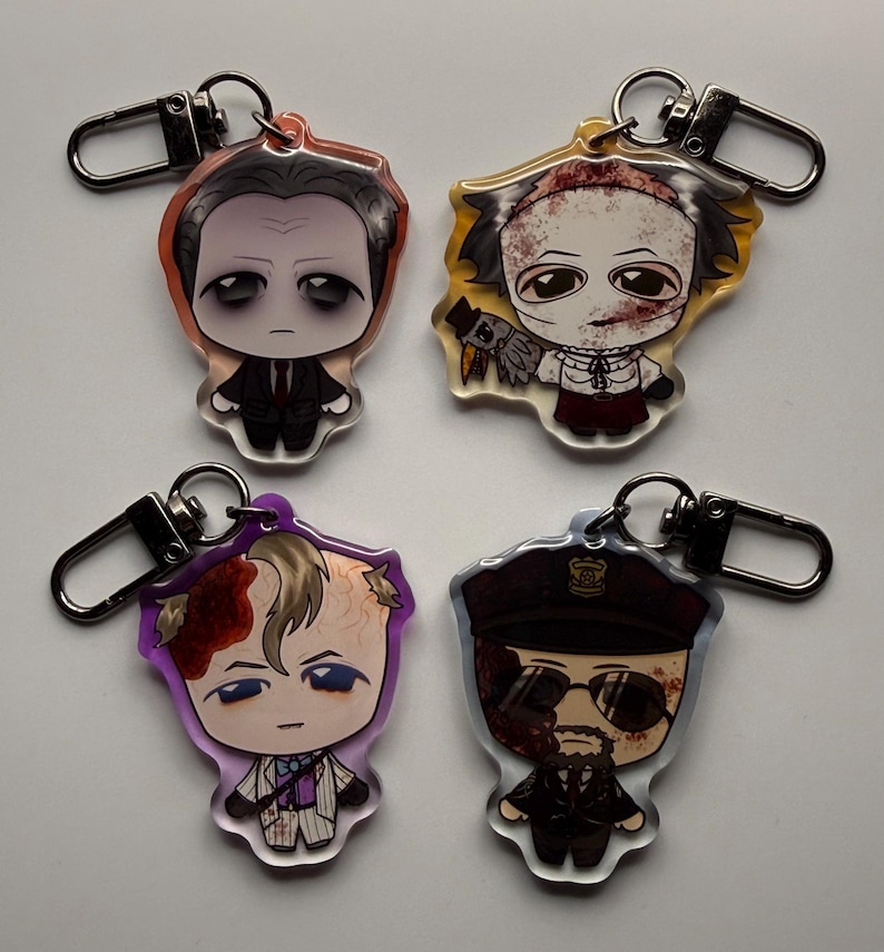 May include: Four acrylic keychains featuring cartoon illustrations of horror movie characters. Each keychain has a silver-colored clasp. The characters are depicted in various outfits and with different facial expressions, with a focus on their distinctive features.