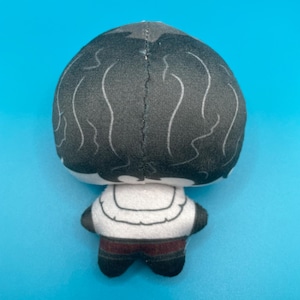 May include: A plush doll with a black head and white wavy lines, a white torso with a curved design, and dark red pants. The doll's back is visible against a bright blue background.