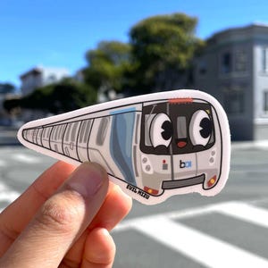May include: A white and blue cartoon train sticker with big eyes and a smiling mouth. The sticker has the text "b.a.r.t." on the side and "EVIL MIZU" at the bottom.