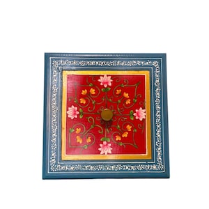 May include: A square wooden box with a blue frame featuring white floral patterns. The center panel is red with a gold border, decorated with painted pink lotus flowers and yellow blossoms, centered by a single round brown knob handle.