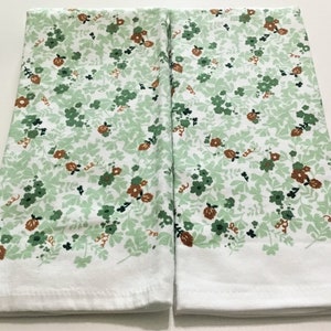 May include: Two white kitchen towels with a green and brown floral pattern. The towels are folded in half and placed side by side.
