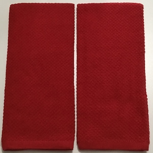 May include: Two red rectangular towels with a textured, woven pattern. The towels are side-by-side, and the color is a vibrant, solid red. The towels are likely for use in a kitchen or bathroom.