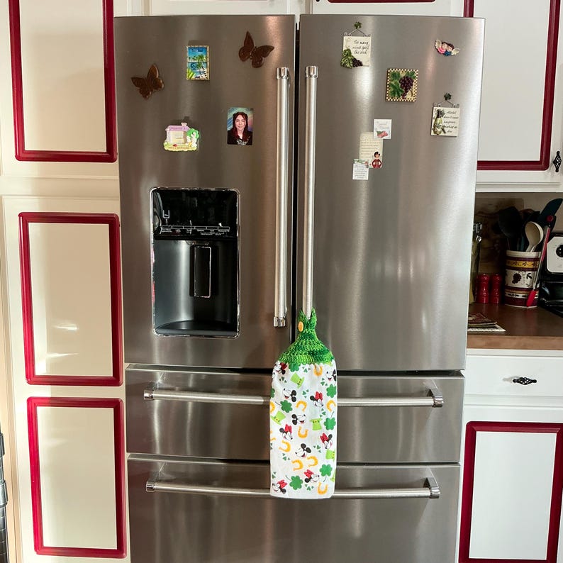 May include: A stainless steel refrigerator with a green and white kitchen towel hanging on the handle. The towel has a shamrock and horseshoe design.
