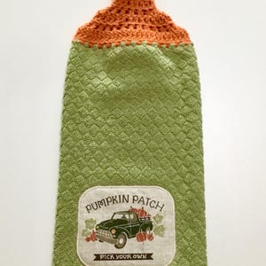 May include: Green kitchen towel with a crocheted orange loop handle and a brown button. The towel has a white patch with a green truck carrying pumpkins and the text "Pumpkin Patch Pick Your Own".