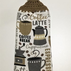 May include: A white kitchen towel with a brown crocheted hanging loop. The towel features a coffee theme with illustrations of coffee cups, a coffee pot, a coffee grinder, and coffee beans. The text on the towel includes "Coffee", "Latte", "Coffee Break", "Cappuccino", and "Espresso".