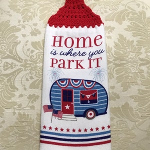 May include: White kitchen towel with a red crocheted hanging loop. The towel features a blue and white camper with red stars and a red door. The text "Home is where you park it" is printed on the towel.