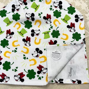 May include: White kitchen towel with a green shamrock, gold horseshoe, and Mickey Mouse and Minnie Mouse print. The towel has a white terry cloth side and a white cotton side with the print. The towel has a tag that says "2 in 1 functionality! Cotton towel for drying dishes and a terry cloth towel for everyday kitchen tasks."