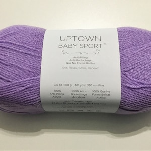 May include: A skein of lavender colored yarn labeled "UPTOWN BABY SPORT™" with the text "Anti-Pilling, Anti-Boulochage, Que No Forma Bolitas, Knit, Relax, Smile, Repeat!" and "3.5 oz | 100 g | 361 yds | 330 m. Fine, 100% Anti-Pilling Acrylic, 100% Anti-Boulochage Acrylique, 100% Que No Forma Bolitas Acrilco, Knit | Tricoter | Tejer, 24 st x 30 rows 4 (3.5 mm)"