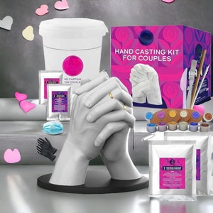 May include: Hand casting kit for couples, featuring two hands clasped together in a white plaster cast. The kit includes two bags of casting powder, a container for mixing, paint, brushes, and gloves. The box has the text "Hand Casting Kit for Couples".